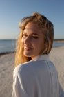 Blonde Frau mit langen Haaren steht am Strand und schaut in die Kamera — Stockfoto
