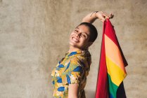 Zufriedene junge bisexuelle ethnische Frau mit bunter Flagge, die LGBTQ-Symbole darstellt und an sonnigen Tagen in die Kamera blickt — Stockfoto