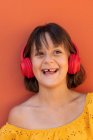 Niño contento escuchando la canción desde auriculares inalámbricos sobre fondo naranja - foto de stock