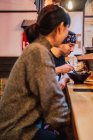 Vue latérale de la femme et de l'homme communiquant tout en mangeant de la nourriture asiatique au comptoir en bois dans un café moderne — Photo de stock