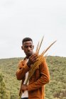 Serious African American male with bunch of dried wheat standing in nature and looking away — Stock Photo