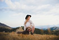 Propriétaire femelle avec chien de hamster obéissant assis dans les montagnes regardant loin — Photo de stock