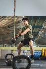Asian man training shoulders and arms with heavy kettlebells in gym during functional workout and looking away — Stock Photo