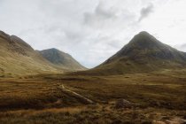 Dirt path on rough grassy hillside in Glencoe, UK countryside on cloudy day — Stock Photo