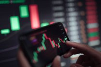 Gesichtsloser Crop Broker mit Mobiltelefon während der Arbeit mit Finanzdiagramm während des Handels — Stockfoto