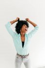 Juguetón joven afroamericano hembra en traje de moda divertirse tocando el pelo afro mirando hacia arriba sobre fondo blanco - foto de stock