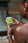 Неузнаваемая афроамериканка просматривает фитнес-приложение на смартфоне, стоя на размытом фоне городской улицы во время тренировки на открытом воздухе. — стоковое фото
