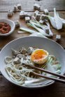 Tagliatelle di ramen fresche e cotte con tofu, uova e verdure servite su una ciotola di ceramica su un tavolo di legno — Foto stock
