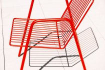 Sedia esterna estiva in metallo rosso posizionata sul pavimento bianco alla luce del sole con ombra — Foto stock