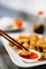 Hand of unrecognizable female using chopsticks to dip yummy wonton into sauce on blurred background of restaurant — Stock Photo