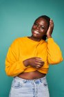 Frohe Afroamerikanerin in gelben Klamotten blickt in die Kamera, die vor blauem Hintergrund steht — Stockfoto