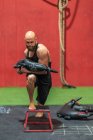 Potente deportista con bolsa pesada pisando y abalanzándose sobre el taburete durante el entrenamiento funcional en el gimnasio moderno - foto de stock