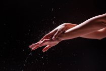 Vista ritaglio di donna anonima lavarsi le mani e l'avambraccio con spruzzi d'acqua su sfondo nero — Foto stock