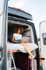 Young African American female traveler with curly hair watching movie on laptop while resting inside camper van during summer holidays — Stock Photo
