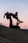 Vista lateral de pareja agraciada haciendo acroyga en el fondo del cielo puesta del sol en las montañas - foto de stock