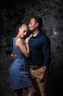 Ніжний етнічний чоловік цілує жінку з закритими очима на фоні темряви в студії — стокове фото
