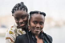 Conteúdo senhoras afro-americanas elegantes que ficam perto e olham para a câmera com um sorriso atencioso no parque em um dia brilhante — Fotografia de Stock