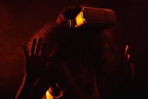 Anonymous astonished ethnic female with open mouth exploring virtual reality in headset on black background — Stock Photo