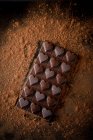 Von oben ganze Schokoriegel mit herzförmiger Dekoration auf schwarzem Hintergrund mit verstreutem Kakaopulver — Stockfoto
