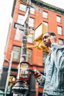 Dal basso allegro contenuto ragazzo afroamericano in denim giacca alla moda surf moderno telefono cellulare durante la passeggiata in città — Foto stock