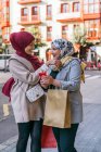 Vue latérale du contenu Des amies musulmanes dans des hijabs se tenant dans la rue et s'embrassant en se regardant — Photo de stock