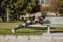 Joven fitness mujer afroamericana haciendo ejercicio después de correr en el banco del parque - foto de stock
