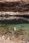 Entspannte Asiatin blickt auf transparentem Wasser des Bimmah Sinkhole, umgeben von rauen Felsen, während ihrer Reise in den Oman in die Kamera — Stockfoto