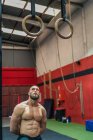 М'язистий бородатий чоловік дивиться вгору, стоячи біля обладнання під час тренування в сучасному тренажерному залі — стокове фото