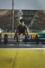 Focalisé asiatique athlète masculin faisant haltérophilie avec haltère lourd pendant l'entraînement dans la salle de gym en regardant la caméra — Photo de stock