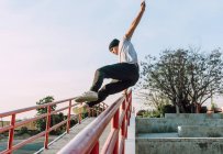 Basso angolo impavido giovane uomo saltare sopra ringhiera metallica in città durante l'esecuzione di acrobazia parkour nella giornata di sole — Foto stock