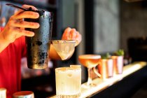 Crépuscule ciblée barman méconnaissable versant cocktail rafraîchissant froid à travers passoire en verre placé sur le comptoir dans le bar — Photo de stock