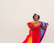 Стильная афроамериканка в модной одежде с красочным флагом, смотрящая в камеру во время празднования — стоковое фото