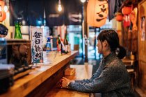Азиатка в повседневной одежде сидит за деревянным столиком, ожидая заказа в рамен-баре — стоковое фото