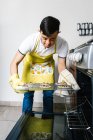 Етнічний хлопчик-підліток з синдромом Дауна кладе сире шоколадне печиво в духовку під час випічки випічки на кухні — стокове фото