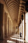 Piena lunghezza di donna irriconoscibile in abiti tradizionali passeggiando attraverso l'arco ornamentale del Sultano Qaboos Grande Moschea di Muscat — Foto stock