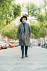Молодой трансгендер в стильном пальто и шляпе смотрит в сторону при дневном свете — стоковое фото
