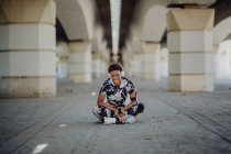 Jovem aptidão afro-americana mulher descansando e esticando as pernas enquanto ouve música depois de correr na rua da cidade — Fotografia de Stock