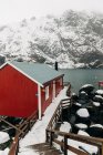 Holzweg in der Nähe einer Barackenmauer in einem Küstenort in der Nähe eines schneebedeckten Bergrückens an einem Wintertag auf den Lofoten, Norwegen — Stockfoto