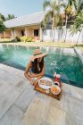 Fröhliche Touristinnen lehnen am Pool und schauen auf Tablett mit leckerem Frühstück im Sonnenlicht — Stockfoto