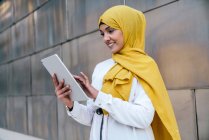 Femme entrepreneur musulmane souriante en hijab jaune debout dans la rue et la tablette de navigation — Photo de stock