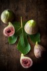 Vue de dessus de figues mûres coupées en deux et entières placées avec des feuilles vertes sur une table rustique en bois — Photo de stock