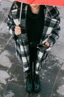 From above young ethnic female in checkered coat browsing cellphone while standing under red umbrella on rainy day on wet street — Stock Photo