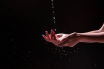 Schnittansicht einer anonymen Frau, die sich vor schwarzem Hintergrund mit Spritzwasser die Hände wäscht — Stockfoto