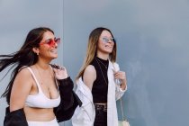 Позитивные подруги в модных солнцезащитных очках и повседневной одежде счастливо смеются, проводя время вместе — стоковое фото