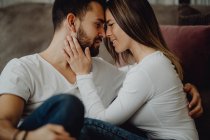 Lächelnde Frau umarmt und küsst fröhlichen Mann auf die Stirn, während er auf dem Boden sitzt — Stockfoto