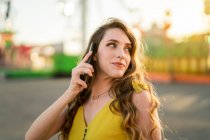 Contenuto femminile parlando sul cellulare mentre in piedi nel parco divertimenti in serata in estate — Foto stock