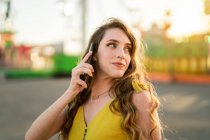 Content female speaking on mobile phone while standing in amusement park in evening in summer — Stock Photo