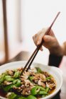 Mão comendo tigela de sopa deliciosa quente com polvo picante e pepino com pauzinhos no café asiático — Fotografia de Stock