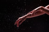Crop view of anonymous woman washing hands and forearm with splashing water against black background — Stock Photo