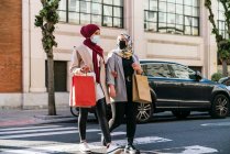 Мусульманські жінки - друзі в масках і з паперовими сумками, які перетинають дорогу, йдучи по місту після покупки. — стокове фото